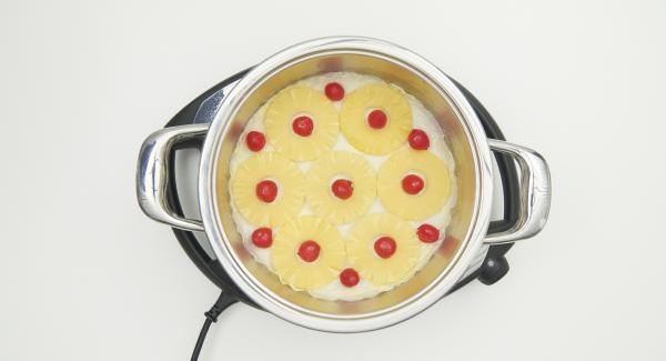 Spread the drained pineapple on the baking paper and fill the gaps with drained cherries, spread the dough over it.