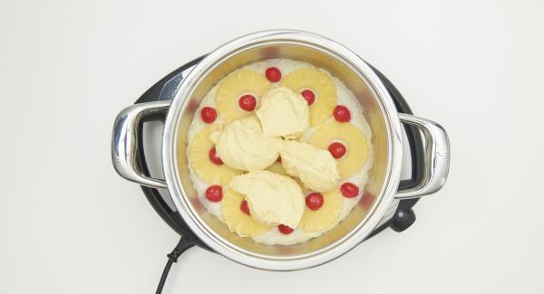 Spread the drained pineapple on the baking paper and fill the gaps with drained cherries, spread the dough over it.